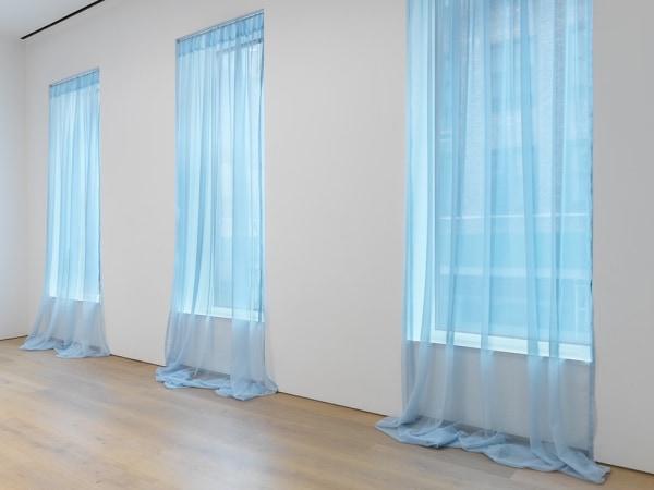 Blue translucent curtains are draped over three big windows. 